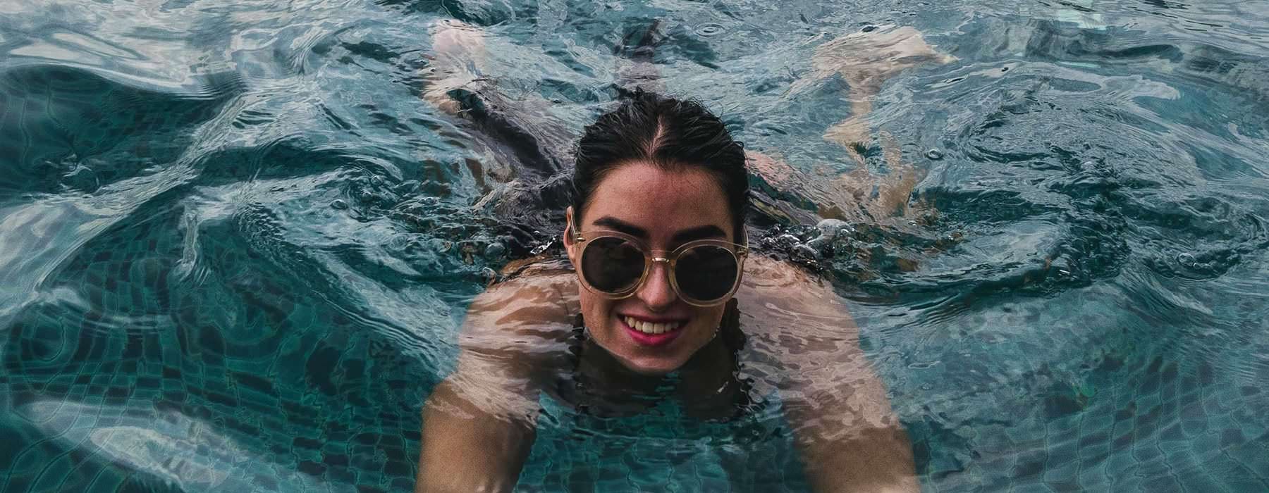 woman with sunglasses, swims in pool